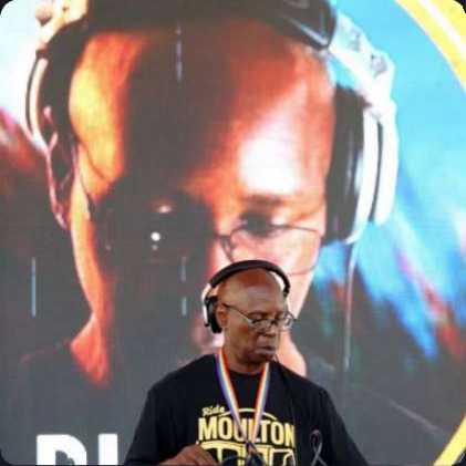 John Parker at the decks in headphones, a large screen behind him showing a close-up of him mixing