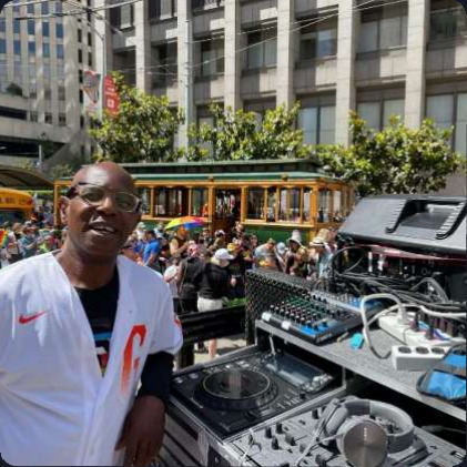 John Parker beside his decks at an outdoor street parade, a cable car and crowd behind him