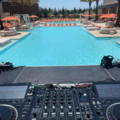 View across a resort pool from behind John Parker's decks, orange parasols and sun loungers around the water